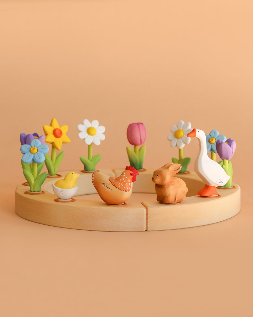 A chick, chicken, rabbit, and goose—wooden spring animal toys—are displayed on the Bumbu Handmade Wooden Celebration Ring with colorful flowers. These eco-friendly toys make a charming addition to any Montessori collection.