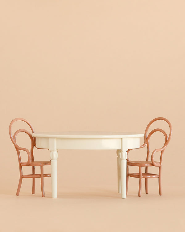 A round white table from the Maileg Dining Table & Chairs Set is paired with two charming brown chairs on either side, all set against a plain beige background.