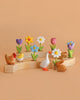 Eco-friendly wooden toys—a chicken with chicks, a goose, and a rabbit—are displayed on the Bumbu Handmade Wooden Celebration Ring, set against a peach background.