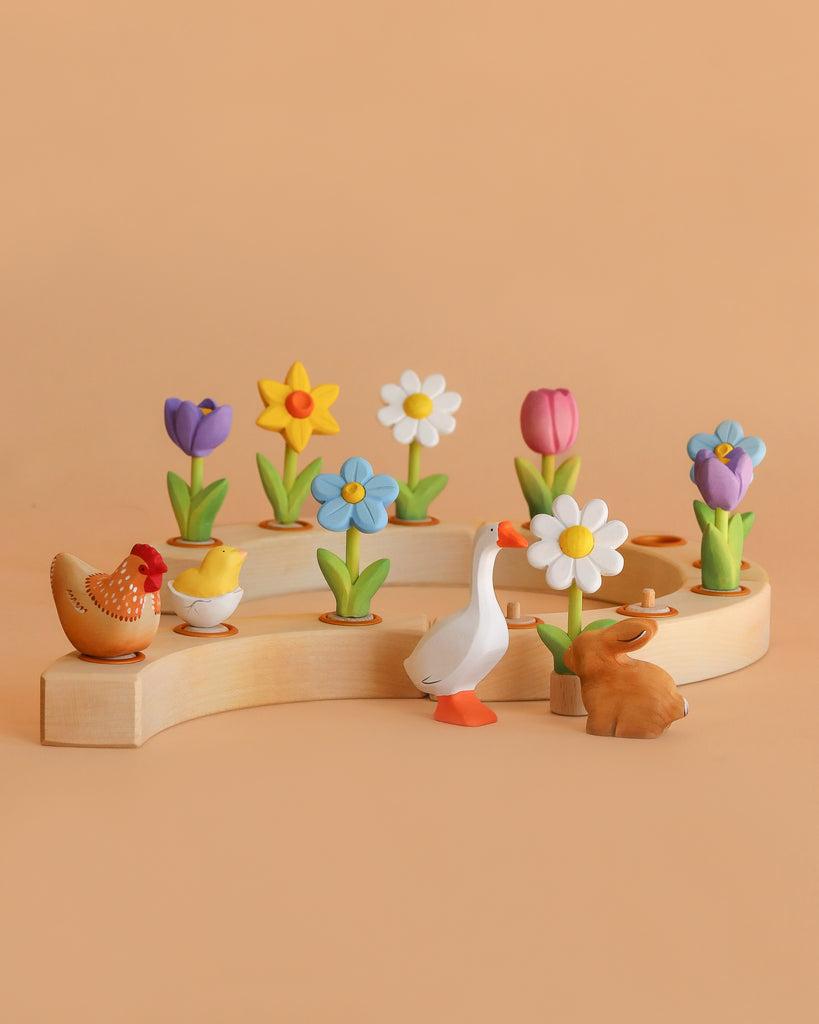 Eco-friendly wooden toys—a chicken with chicks, a goose, and a rabbit—are displayed on the Bumbu Handmade Wooden Celebration Ring, set against a peach background.