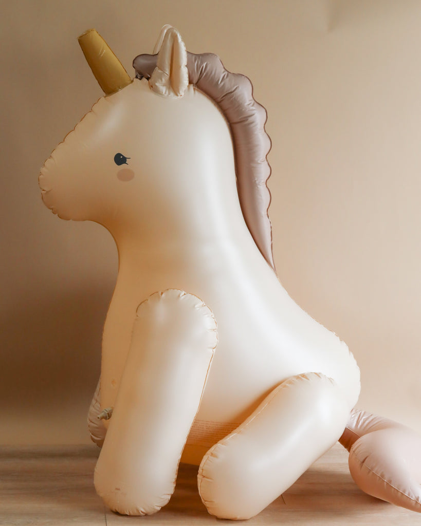 Inflatable Giant Unicorn Sprinkler with a golden horn and beige mane, made from durable PVC, sitting upright against a plain, warm-toned background.