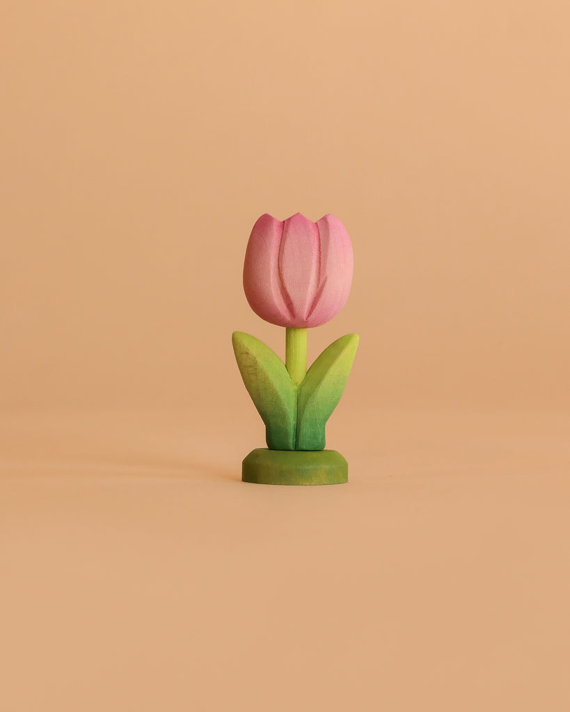 The Bumbu Handmade Wooden Flower Festive Tulip is a pink wooden tulip with green leaves on a green base—an eco-friendly piece perfect for Montessori toy collections, pictured against a plain beige background.