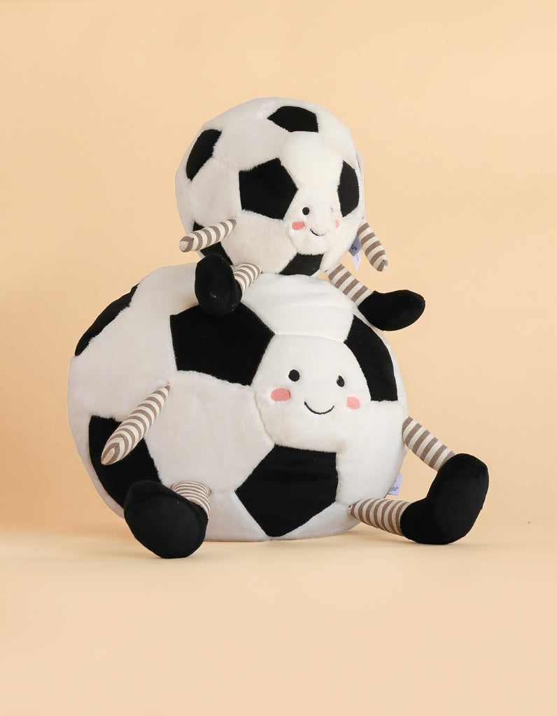 Two Mon Ami Sergio Soccer Ball plush toys with smiling faces, rosy cheeks, striped arms and legs, and black feet are sitting against a plain beige background—a perfect soccer gift for any fan.