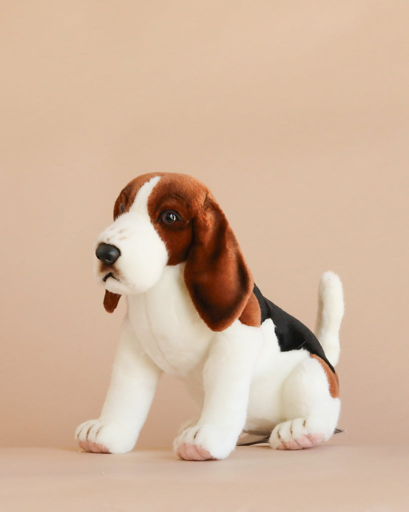 A hand-sewn Beagle Dog Stuffed Animal with brown, black, and white fur sits against a plain beige background, showcasing realistic features that make it stand out among plush animals.