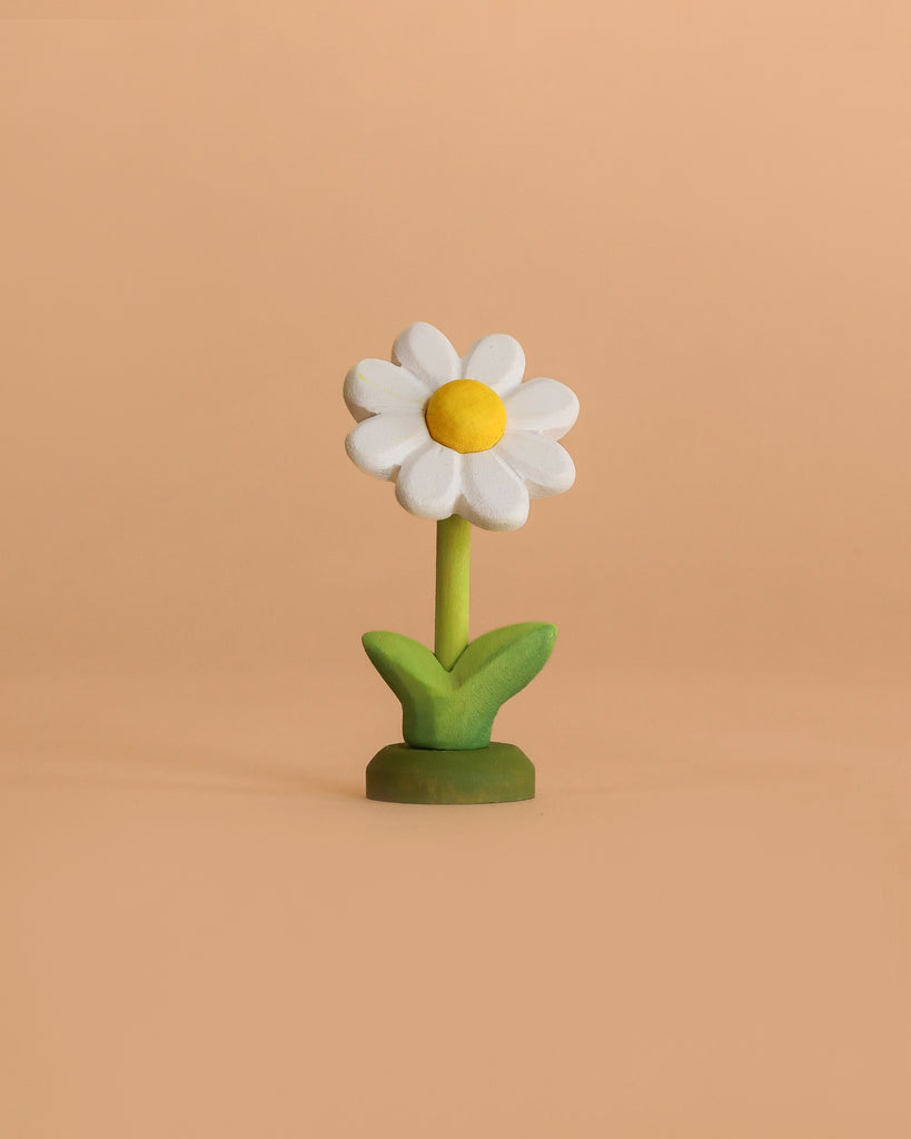 The Bumbu Handmade Wooden Flower Festive Daisy features a yellow center and green leaves, standing upright on a beige background—ideal for a Montessori Waldorf celebration ring.