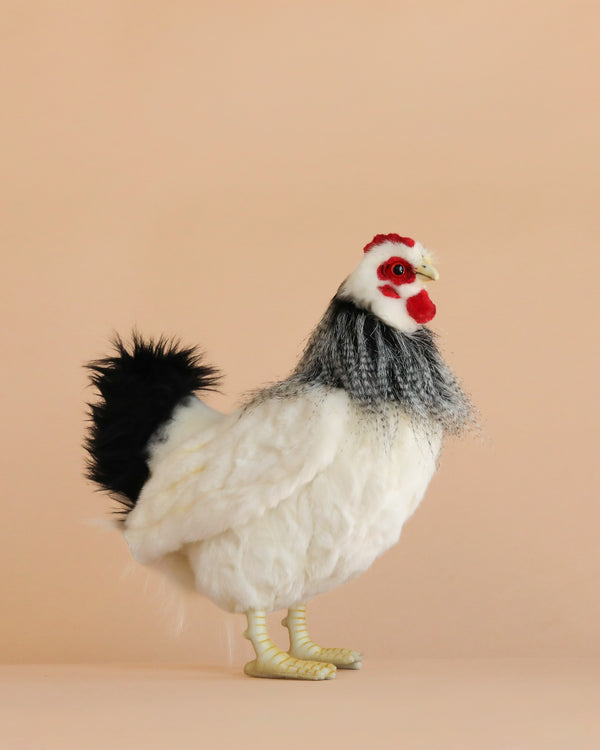 A French White Hen Stuffed Animal with black tail feathers and a red comb stands on a neutral beige background, facing right and displaying the lifelike details that are often admired in hand sewn plush toys.