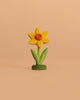 The Bumbu Handmade Wooden Flower Festive Daffodil features a yellow bloom with an orange center and green stem, standing upright on a light beige background—ideal for imaginative play or as a charming display in celebration rings.