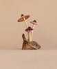 The Small Wooden Purple Mushroom Trio features three handcrafted wooden mushrooms, each with brown stems and dark purple caps edged in pink, growing from a piece of brown wood. This decorative figurine rests on a driftwood base, set against a light beige background for a minimalist and natural look.