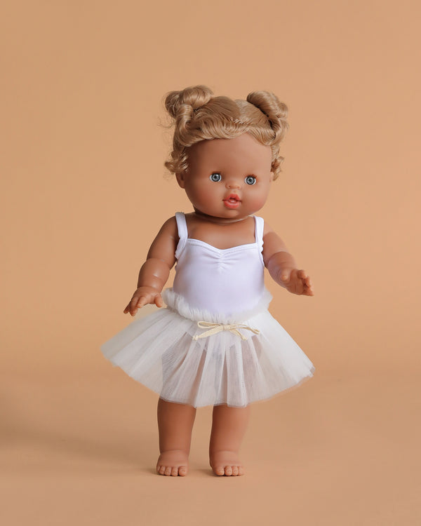 The Minikane Standing Doll (14") – Louisa with Clothing features brown hair, blue eyes, and a white ballerina outfit with tulle skirt. This barefoot, anatomically correct doll is beautifully made in Spain and poses against a beige background.