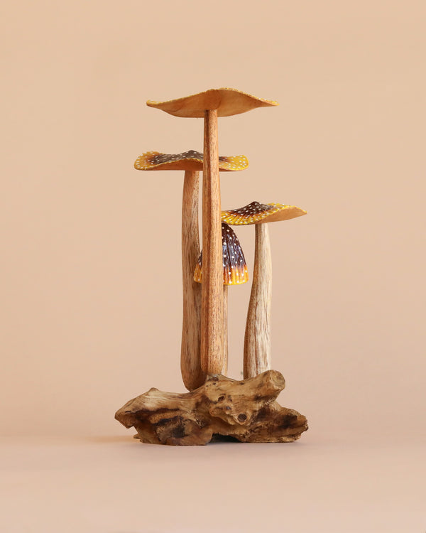 A trio of small, natural wooden mushrooms with textured stems and caps, arranged on a driftwood base and set against a plain beige background.