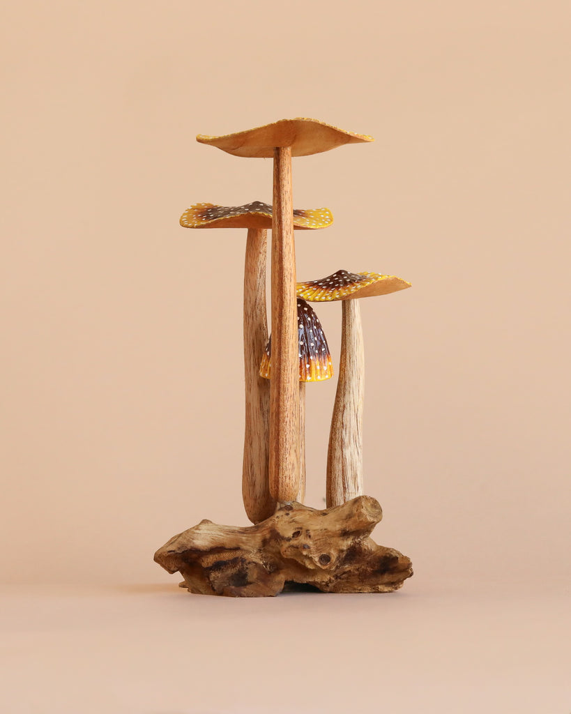 A trio of small, natural wooden mushrooms with textured stems and caps, arranged on a driftwood base and set against a plain beige background.
