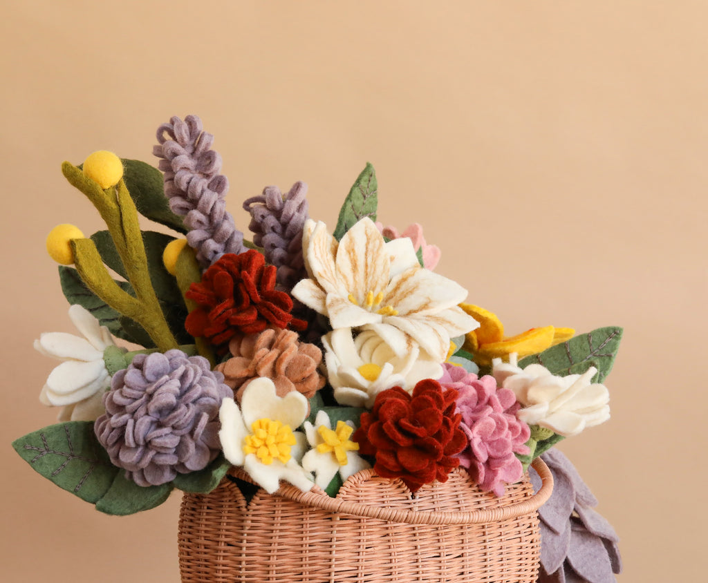 Introducing the “Basket of Felt Flowers - Final Sale”: a woven basket brimming with an eco-friendly, wool felt bouquet. This vibrant floral display showcases colorful felt flowers in red, white, yellow, purple, and pink blooms, all beautifully arranged against a plain beige background.