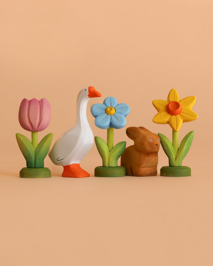 The Bumbu Handmade Wooden Spring Set features a pink tulip, white goose, blue flower, brown rabbit, and yellow daffodil arranged on a peach background—ideal Montessori toys for eco-friendly play.