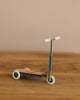 The Maileg Mouse Size Scooter/Kickboard - Blue features a wooden deck and white wheels, sitting elegantly on a wooden surface, accentuated against a plain beige background.