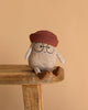 The Spud Bud Potato Plush Toy, featuring glasses, a red knit hat, and brown shoes, sits on a wooden bench against a beige background—a quirky and cuddly gift idea.