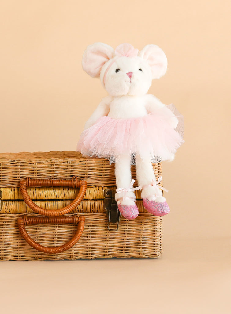 A Bukowski - Antonia Mouse - White plush toy dressed in a pink tutu and ballet shoes sits on a wicker basket against a beige background.