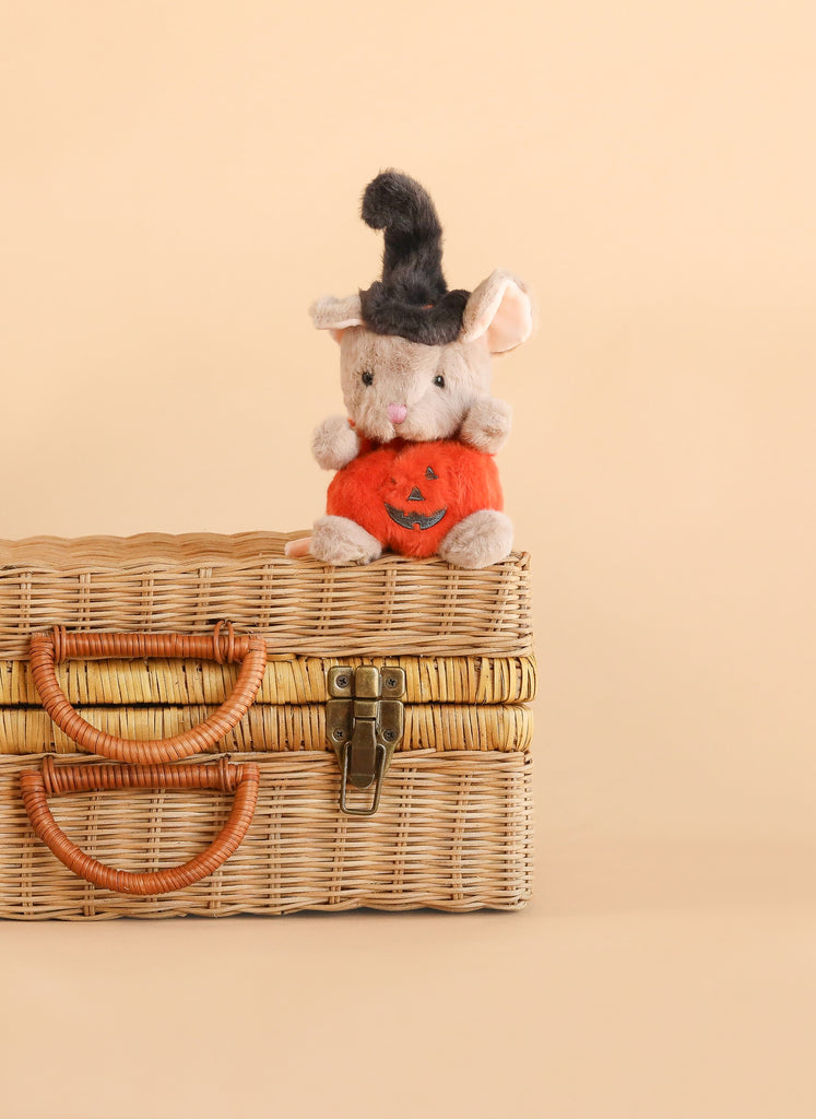 Bukowski - Mousy Pumpkin, a small Halloween stuffed animal mouse plush wearing a black witch hat and holding an orange pumpkin, sits atop a wicker basket with leather handles against a plain beige background.