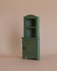 The Maileg Cozy Evening with Granddad Set includes a small green wooden cabinet with two open shelves and a closed door with a knob, ideal as dollhouse furniture.