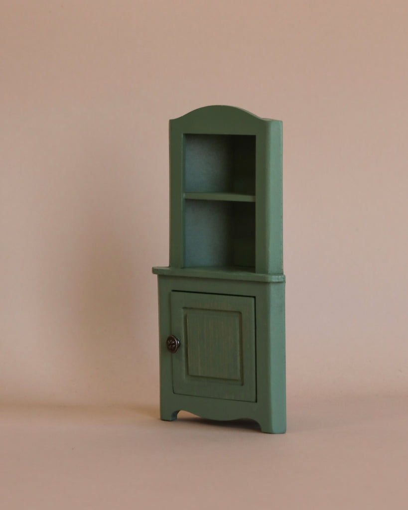 The Maileg Cozy Evening with Granddad Set includes a small green wooden cabinet with two open shelves and a closed door with a knob, ideal as dollhouse furniture.