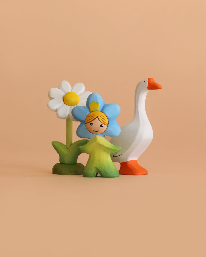 The Bumbu Handmade Wooden Spring Set features a girl in a blue costume with a yellow crown, a white daisy, and an orange-beaked goose—eco-friendly figurines perfect for Montessori play on a plain beige background.
