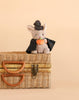 A Bukowski - Mousy Witch plush, dressed in a black cape and hat and holding a pumpkin, sits atop a woven picnic basket against a beige background.