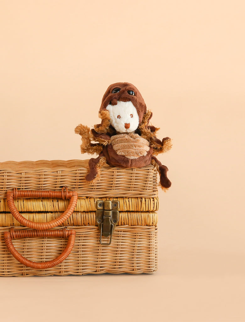 The Bukowski - Ziggy Spider plush toy, featuring a white face, sits atop a closed wicker picnic basket against a plain beige background, inviting imaginative play.