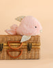 Mon Ami - Crystal the Fish Plush Toy, a soft pink stuffed animal with shiny fins, sits atop a closed wicker suitcase against a beige background. This tropical fish plush makes an adorable gift for kids.