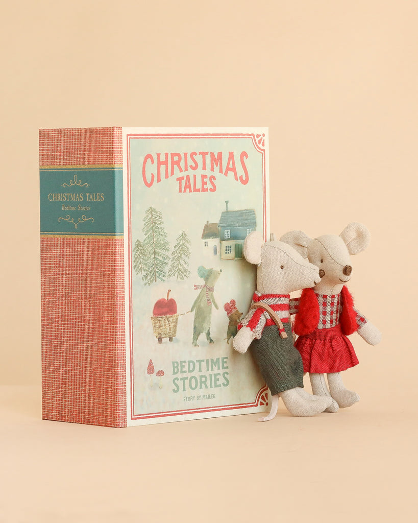 A book titled “Christmas Tales Bedtime Stories” stands upright next to the charming Maileg Christmas Twins Set—two plush mice dressed in festive red and grey outfits, perfectly Mouse Size—all set against a soft beige background.