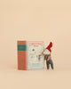 A delightful Maileg Christmas Mouse, Baby in Book, wearing a red hat, stands next to the “Christmas Tales: Bedtime Stories” illustrated book featuring two sweet mice on the cover, all set against a simple beige background.