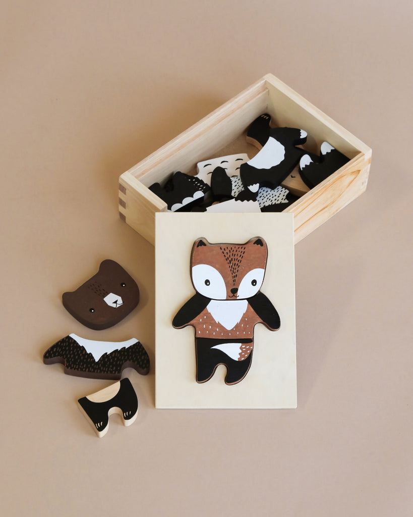 A wooden puzzle of a fox with interchangeable pieces, displayed alongside a wooden box containing various black and white Mix & Match Animal Tiles, set on a beige background.