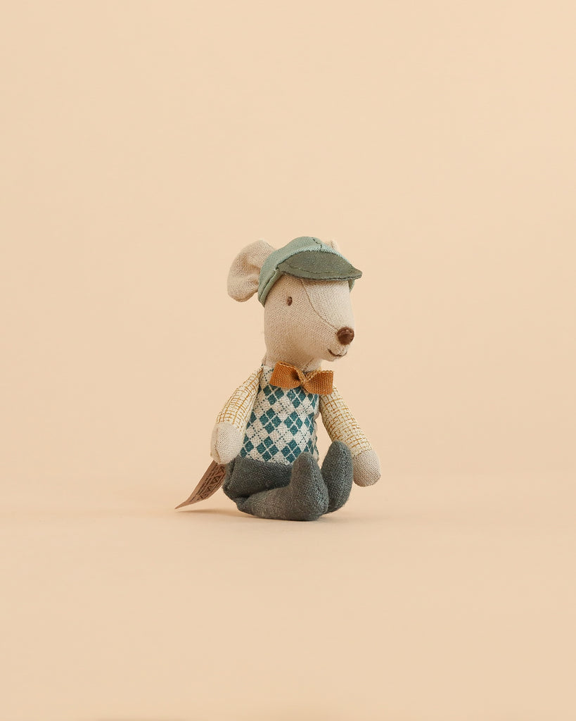 The Maileg Driver Mouse, Little Brother plush toy—dressed in a green cap, argyle vest, orange bow tie, and blue pants—sits upright on a beige background.