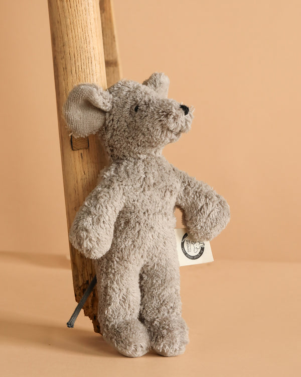 The Senger Naturwelt Stuffed Animal - Mouse stands upright by a wooden ladder, featuring a small side tag. Made from GOTS-certified materials, it's a charming, sustainable decor piece set against a beige background.