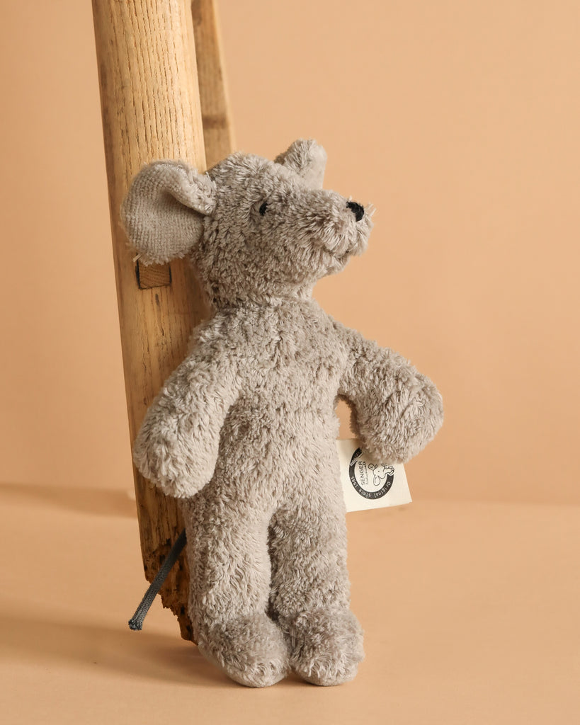 The Senger Naturwelt Stuffed Animal - Mouse stands upright by a wooden ladder, featuring a small side tag. Made from GOTS-certified materials, it's a charming, sustainable decor piece set against a beige background.