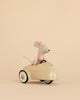A Maileg Little Sister Driver Set, featuring a small mouse in a pink dress with a flower headband, is displayed sitting in a cream-colored car against a plain beige background.