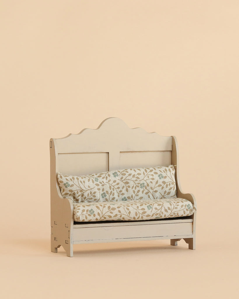The Maileg Kitchen Bench, Mouse - Light Sand is a small wooden bench featuring a decorative backrest and soft, floral-patterned cushions, set against a plain beige background to create an inviting and cosy atmosphere.