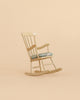 A Maileg Cozy Christmas Corner light wooden rocking chair with a patterned seat cushion, perfect for Maileg mouse furniture, sits on a plain beige background.