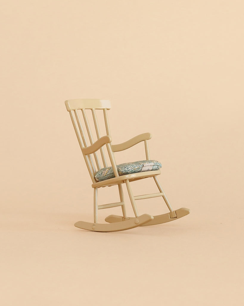 A Maileg Cozy Christmas Corner light wooden rocking chair with a patterned seat cushion, perfect for Maileg mouse furniture, sits on a plain beige background.