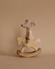 A small, handcrafted fabric mouse toy wearing a patterned outfit is seated on a Small Handmade Wooden Rocking Horse against a neutral brown background. The rocking horse has a smooth, natural finish enhanced with linseed oil, complementing the soft colors of the mouse toy.