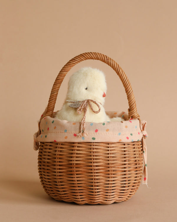 A plush white chick peeking out of a Rattan Berry Basket With Lining – Gumdrop against a soft beige background.