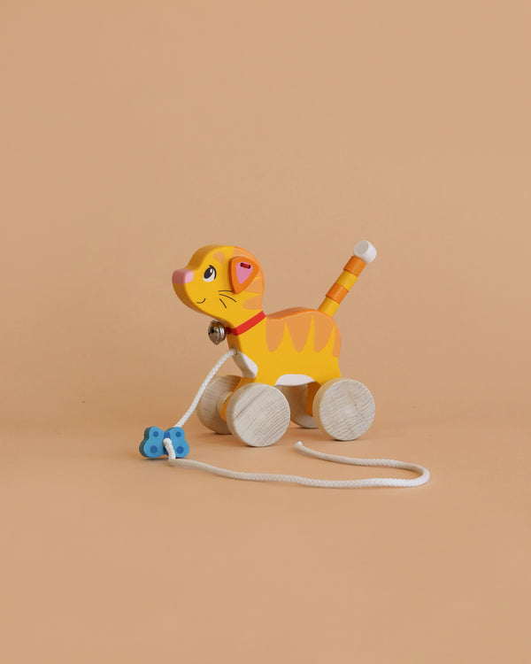 The Holztiger Pull-Along Cat is a wooden toy shaped like an orange tiger with yellow stripes, a pink nose, and a blue bone-shaped handle—an adorable toddler toy set against a plain beige background.