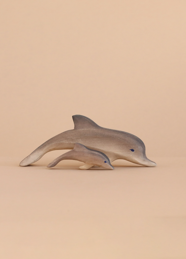 Two handcrafted toys from the Bumbu Handmade Wooden Dolphin Family Set, featuring an adult and calf dolphin, are displayed side by side on a light beige background to highlight their eco-friendly design.