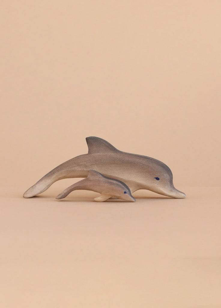 Two handcrafted toys from the Bumbu Handmade Wooden Dolphin Family Set, featuring an adult and calf dolphin, are displayed side by side on a light beige background to highlight their eco-friendly design.