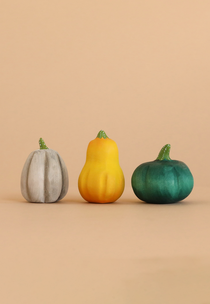 Three small gourds—one gray, one yellow, and one dark green—from the Bumbu Handmade Wooden Pumpkin Patch Set are arranged in a row on a light beige background.