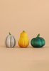 Three small gourds—one gray, one yellow, and one dark green—from the Bumbu Handmade Wooden Pumpkin Patch Set are arranged in a row on a light beige background.