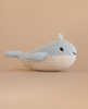 The Cuddle + Kind Baby Whale is a light blue and cream knitted plush toy with a small tail and smiling face, handmade in Peru, shown on a plain beige background.