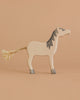The Holztiger Grey Horse, Head Raised is a handcrafted wooden toy with simple painted details, gray mane, and rope tail, standing on a beige surface—a charming example of European craftsmanship.