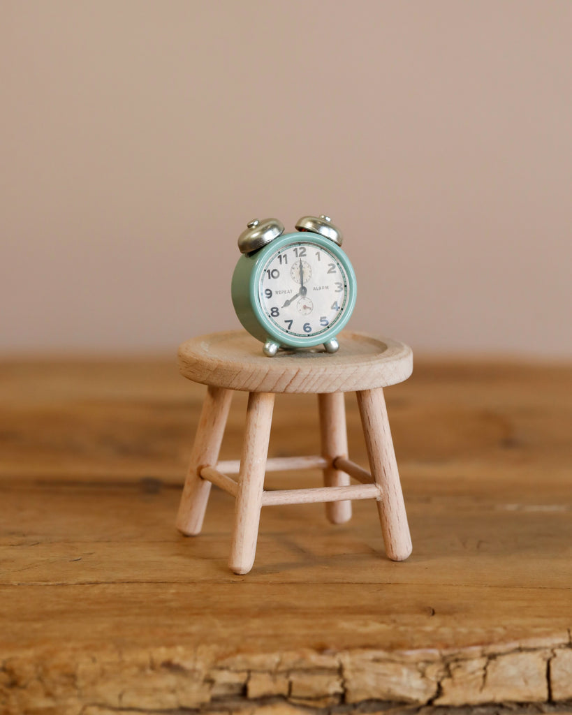 A charming Maileg On The Go Suitcase Set rests on a miniature wooden stool atop a wooden surface, set against a plain beige background—an adorable scene perfect for any Maileg Dollhouse.