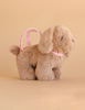 The Konges Sloejd Puppy Bag is a plush toy dog with floppy ears and a pink heart-printed strap, pictured on a neutral beige background.