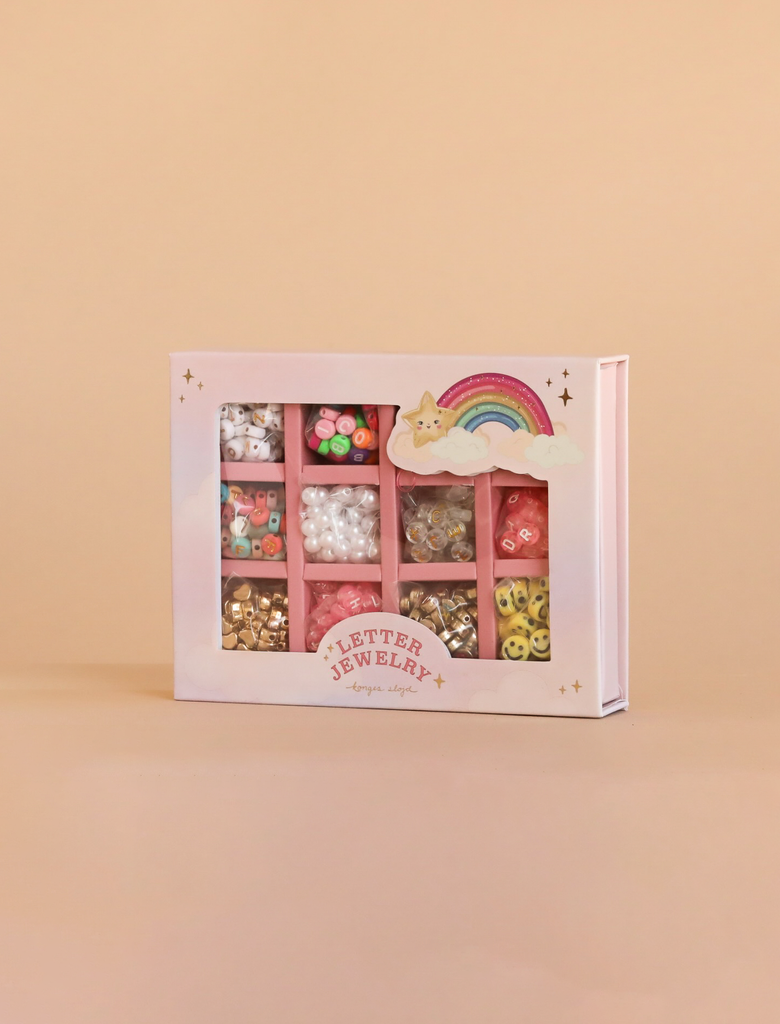 The Konges Sloejd ABC Jewelry Set includes colorful letter, heart, pearl, and smiley face beads—ideal for any jewellery making kit. The pink box has a rainbow, clouds, and stars on a beige background.