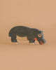 A Holztiger Hippopotamus, Feeding figure—handcrafted from wood and painted in dark gray, white, and orange—stands on a light beige background.